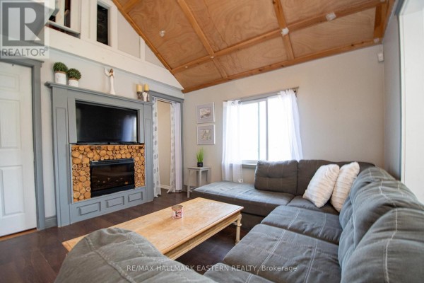 Living room with a sectional sofa, fireplace, coffee table, and a large wood-paneled ceiling. - 2305 Thurstonia Road, Kawartha Lakes