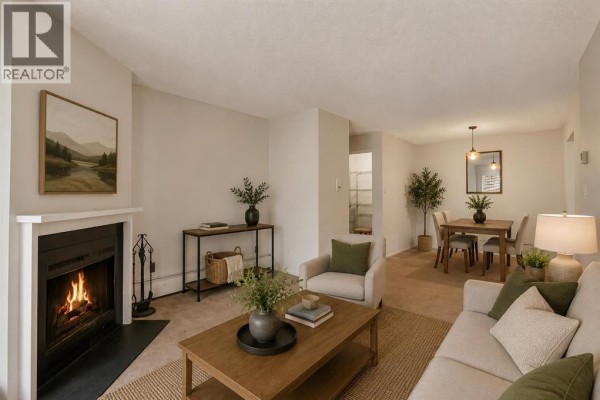 Living room with a fireplace, beige sofa, armchair, coffee table, and dining area visible. - 2306, 315 Southampton Drive Sw, Calgary