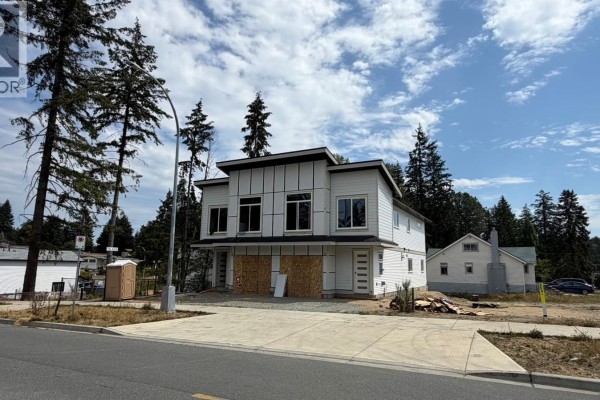 Side exterior view of a modern duplex construction with trees and adjacent buildings. - 2306 Sparrow Lane, Nanaimo