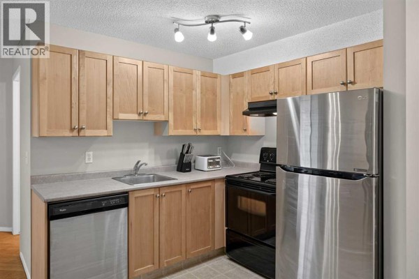 Corner kitchen with light wood cabinets, stainless steel refrigerator, and dishwasher. - 2307, 2518 Fish Creek Boulevard Sw, Calgary