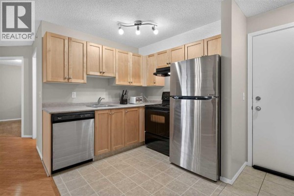 Apartment kitchen with light wood cabinets, stainless steel refrigerator, and dishwasher. - 2307, 2518 Fish Creek Boulevard Sw, Calgary