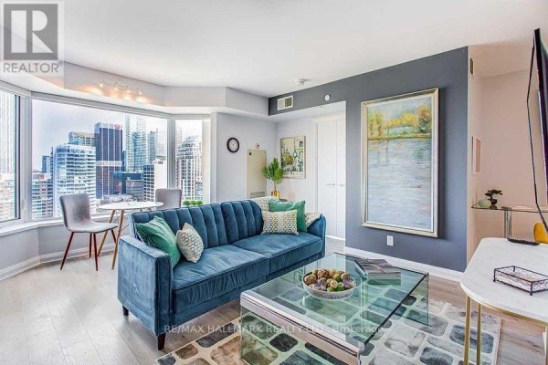 Living room with a blue sofa, artwork, and large windows showcasing the skyline. - 2307 - 155 Yorkville Avenue, Toronto