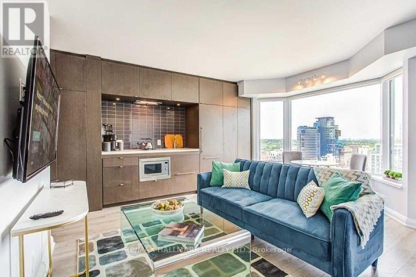 Modern kitchen area with dark cabinetry, microwave, and a view of the city. - 2307 - 155 Yorkville Avenue, Toronto