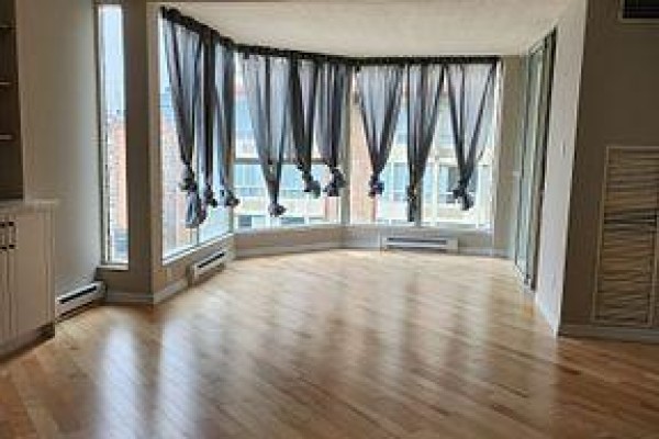 Living room with hardwood floors, large bay windows, and grey curtains. - 2307 - 55 Centre Avenue, Toronto