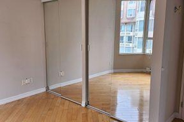Bedroom with hardwood floors and a wall of mirrored closet doors. - 2307 - 55 Centre Avenue, Toronto