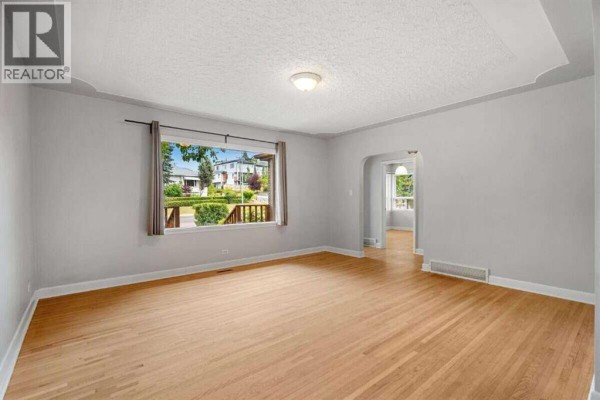 Living room with light grey walls, hardwood floors, and a large picture window overlooking the street. - 2307 Richmond Road Sw, Calgary