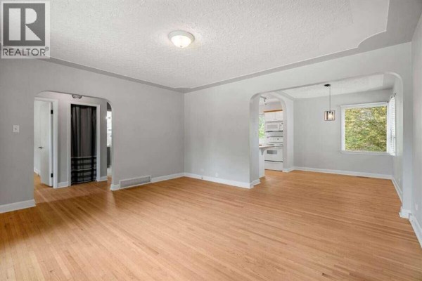 Interior view of the main living area, showing archways to other rooms, hardwood floors, and a glimpse of the kitchen. - 2307 Richmond Road Sw, Calgary