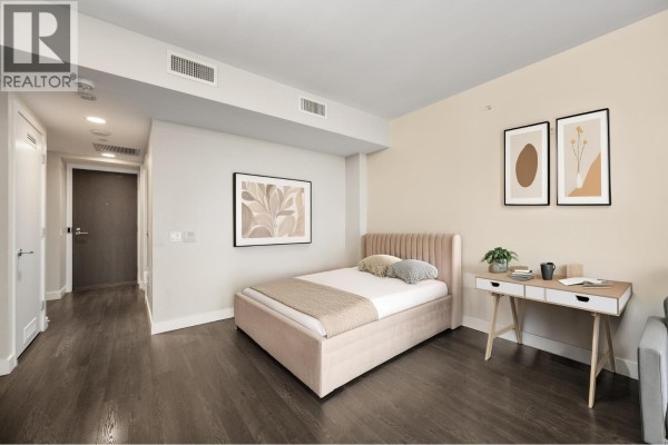 Bedroom featuring a bed frame, desk, and neutral decor with hallway access. - 2308 2008 Rosser Avenue, Burnaby