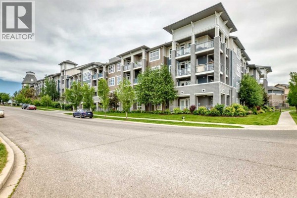 Side view of a multi-story apartment building with balconies, trees, and a paved walkway. - 231, 25 Auburn Meadows Avenue Se, Calgary