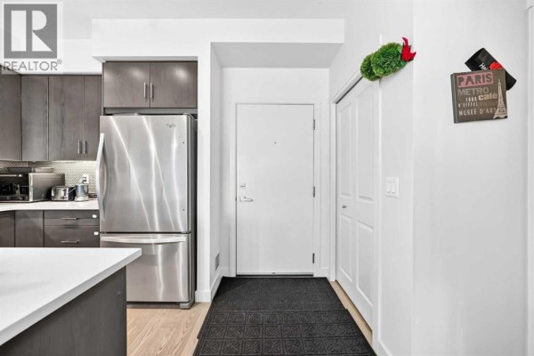 Apartment entryway with a stainless steel refrigerator, dark wood cabinets, and a white door. - 231, 25 Auburn Meadows Avenue Se, Calgary