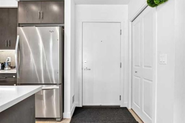 Apartment entryway showing a white door with a peephole, a closet, and a stainless steel refrigerator. - 231, 25 Auburn Meadows Avenue Se, Calgary