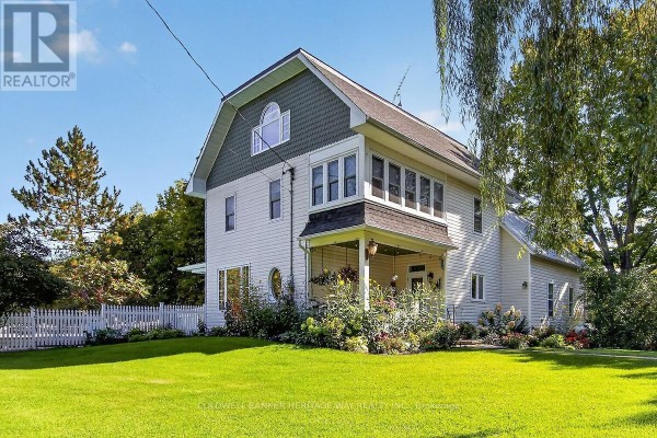 Side view of the white two-story house featuring green shingled gables and a covered front porch with a white picket railing. - 231 Boyds Road, Lanark Highlands