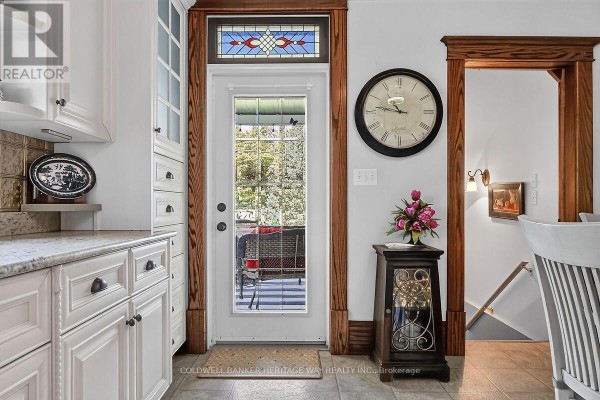 Kitchen interior with white cabinets, granite countertops, a decorative clock, and a glass door leading to a covered outdoor seating area. - 231 Boyds Road, Lanark Highlands