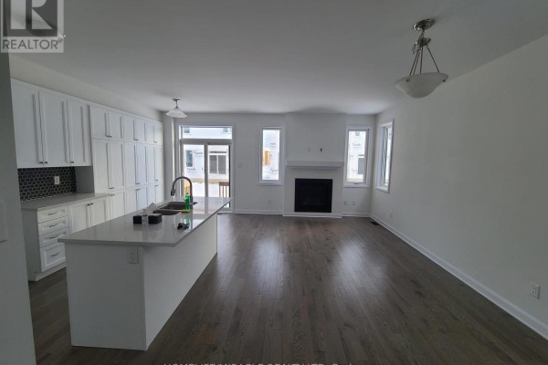 Open concept living area with dark wood floors, fireplace, and white kitchen cabinets. - 231 Clonrush Way, Ottawa