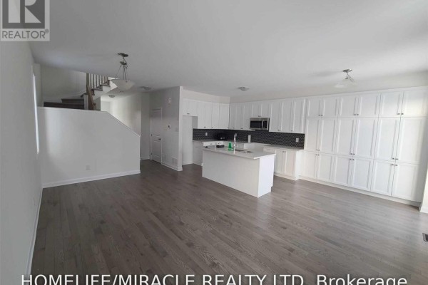 Living area and kitchen with dark wood floors, white cabinets, and a central island. - 231 Clonrush Way, Ottawa