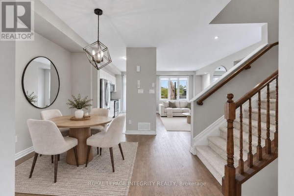 Dining area with a round wood table, four chairs, a large mirror, and staircase leading upstairs. - 231 Mountain Sorrel Way, Ottawa