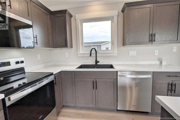 Kitchen corner showing a white sink, black faucet, stainless steel dishwasher, and grey cabinetry. - 231 Rue Bella Vista, Tracadie