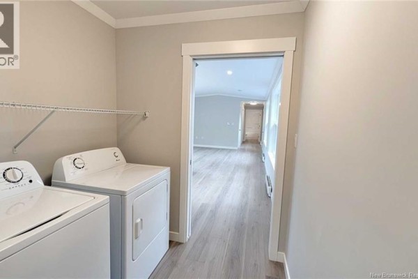 Laundry room with white washer and dryer, looking into a hallway with light grey walls and wood-look flooring. - 231 Rue Bella Vista, Tracadie