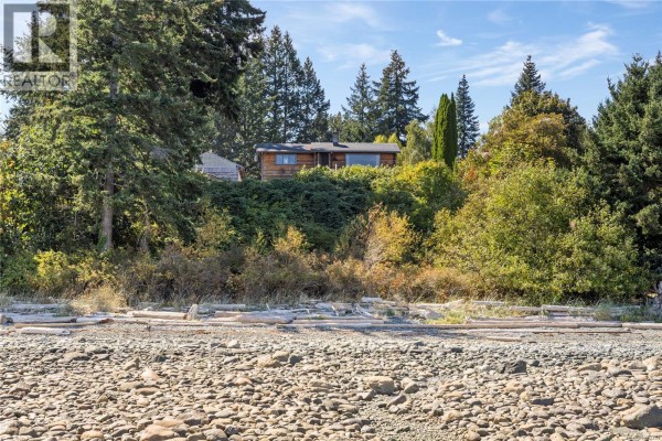 View of the house from the rocky beach with surrounding trees. - 2310 Seabank Rd, Courtenay