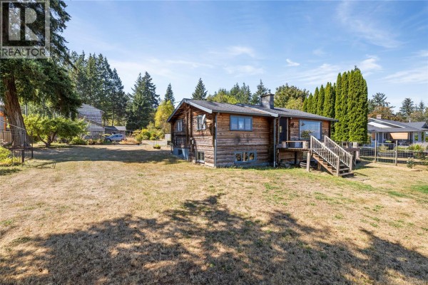 Exterior shot of the log house with a dry grass yard and trees. - 2310 Seabank Rd, Courtenay