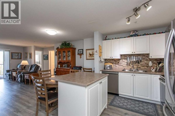 Apartment kitchen with white cabinets, island, dining area, and living room access. - 2311, 12b Ironside Street, Red Deer