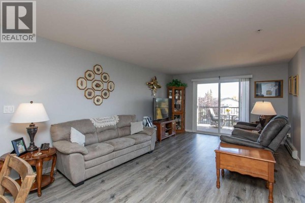 Apartment living room with sofa, chairs, entertainment unit, and balcony access. - 2311, 12b Ironside Street, Red Deer