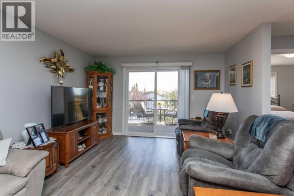 Apartment living area with television, chairs, sofa, and balcony access. - 2311, 12b Ironside Street, Red Deer