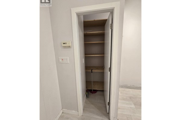 Open closet with wooden shelves and a mop and broom inside. - 2311 4500 Kingsway, Burnaby