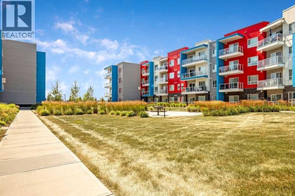 Grassy courtyard with a pathway and picnic table, surrounded by colourful apartment buildings. - 2313, 19489 Main Street Se, Calgary