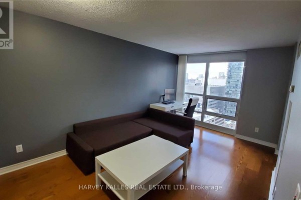 Living area with a dark sofa, white coffee table, desk, and city view window. - 2313 - 763 Bay Street, Toronto