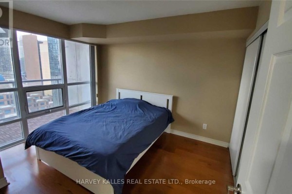 Bedroom with a bed, blue comforter, closet, and large window with city view. - 2313 - 763 Bay Street, Toronto