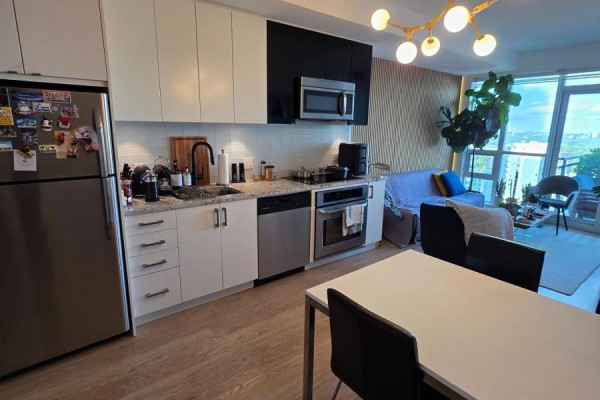 Kitchen with stainless steel appliances, black and white cabinetry, and a dining table in the foreground. - 2316 - 98 Lillian Street, Toronto