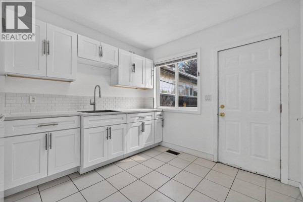 White kitchen cabinets with a grey tiled backsplash, a black sink, and white countertops. - 2316 Nanaimo Street, Vancouver