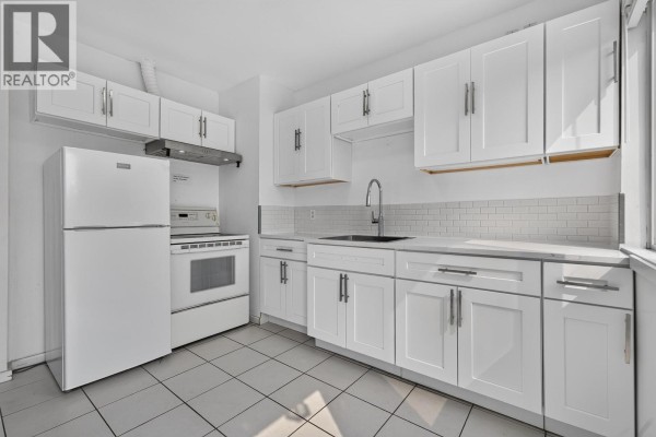 White kitchen with white appliances, white cabinets, grey tiled backsplash, and white countertops. - 2316 Nanaimo Street, Vancouver