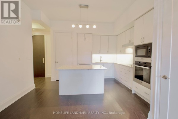 Kitchen area with white cabinets, island, and adjacent living space. - 232 - 20 Fred Varley Drive, Markham