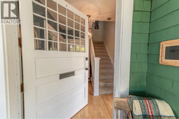 Open front door showing a white-paneled door, hallway with stairs, and green exterior siding. - 232 10th Avenue S, Cranbrook