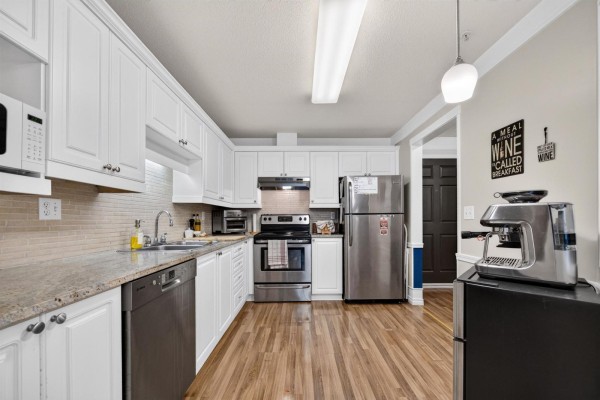 White kitchen with granite countertops, stainless steel appliances, and wood laminate flooring. - 232 8068 120a Street, Surrey
