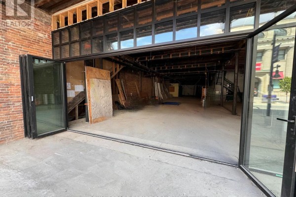 Interior of an empty commercial space with exposed brick walls, wooden beams, and open folding glass doors. - 232 Front Street, Belleville