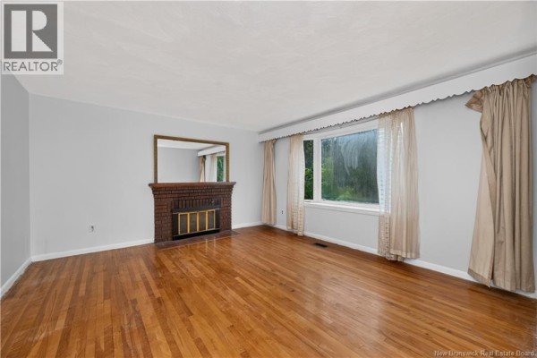 Living room featuring a brick fireplace, wood floors, striped wallpaper, and large beige curtains. - 232 Leslie Street, Moncton