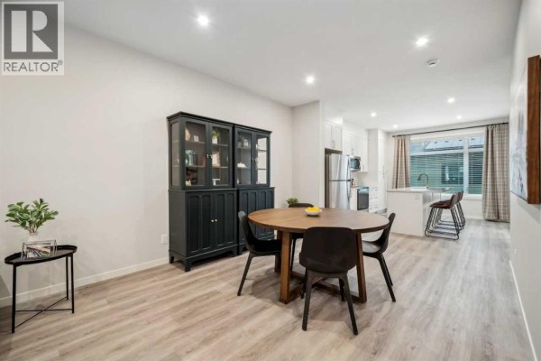 Dining area with round wooden table and chairs, adjacent to white kitchen. - 232 Vantage Drive, Cochrane
