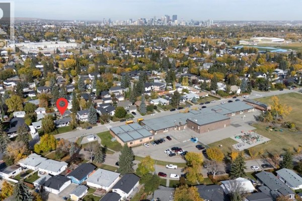 Aerial view showing the property near a school, park, and distant city skyline. - 2320 58 Avenue Sw, Calgary