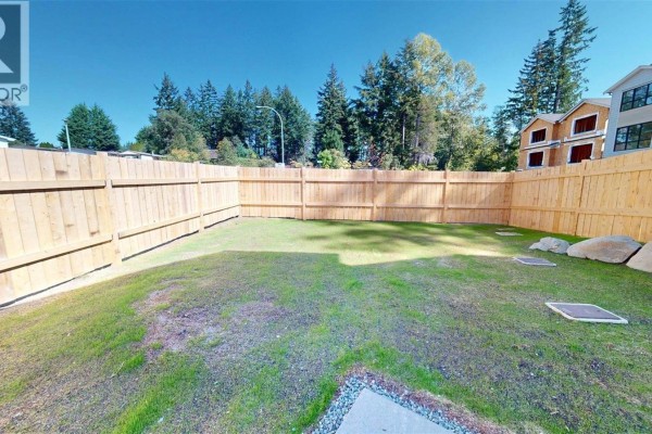 Spacious, level backyard surrounded by a new wooden fence with scattered large rocks. - 2322 Sparrow Lane, Nanaimo