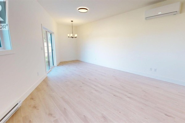 Open concept living area with white walls, light wood floors, and sliding glass door. - 2322 Sparrow Lane, Nanaimo