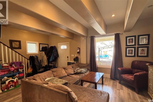 Living room with a sectional sofa, armchair, wood coffee table, and a window with dark curtains. - 2324 Halifax Street, Regina