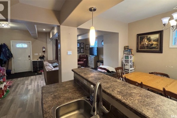 View from kitchen counter showing dining area, living room, and a staircase with a closed door. - 2324 Halifax Street, Regina