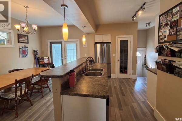 Kitchen island with a sink, stainless steel refrigerator, dining table, and doors leading outside. - 2324 Halifax Street, Regina