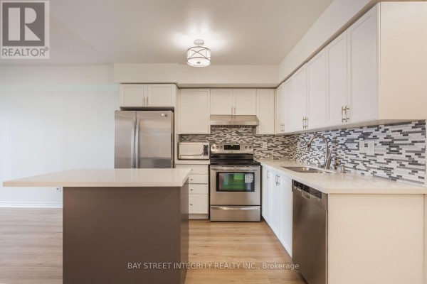 Modern kitchen with white cabinets, stainless steel appliances, and a grey island with a white countertop. - 2328 - 3888 Duke Of York Boulevard, Mississauga