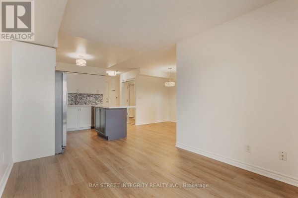 Living room and kitchen area with light wood floors, white walls, and a modern light fixture. - 2328 - 3888 Duke Of York Boulevard, Mississauga
