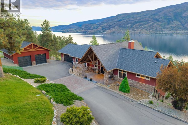 Gated entrance with stone pillars and a winding driveway surrounded by trees. - 2328 Arthur Court, Kelowna