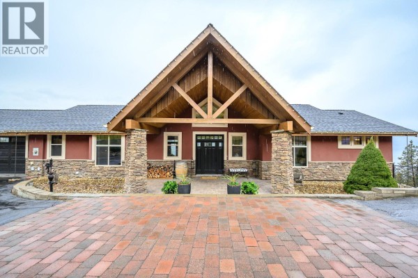 Close-up of the entrance with a wooden door, stone accents, and paver walkway. - 2328 Arthur Court, Kelowna